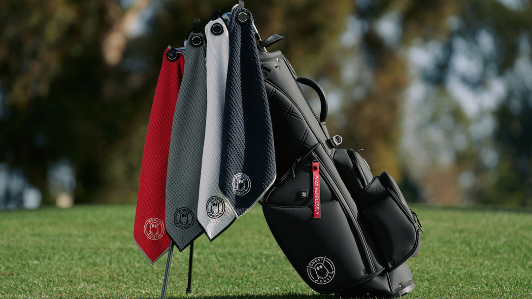 Back Golf Bag on its Legs with 4 Magnetic Golf Towels Stuck on the Golf Clubs. Red, Grey, White and Black Towels.