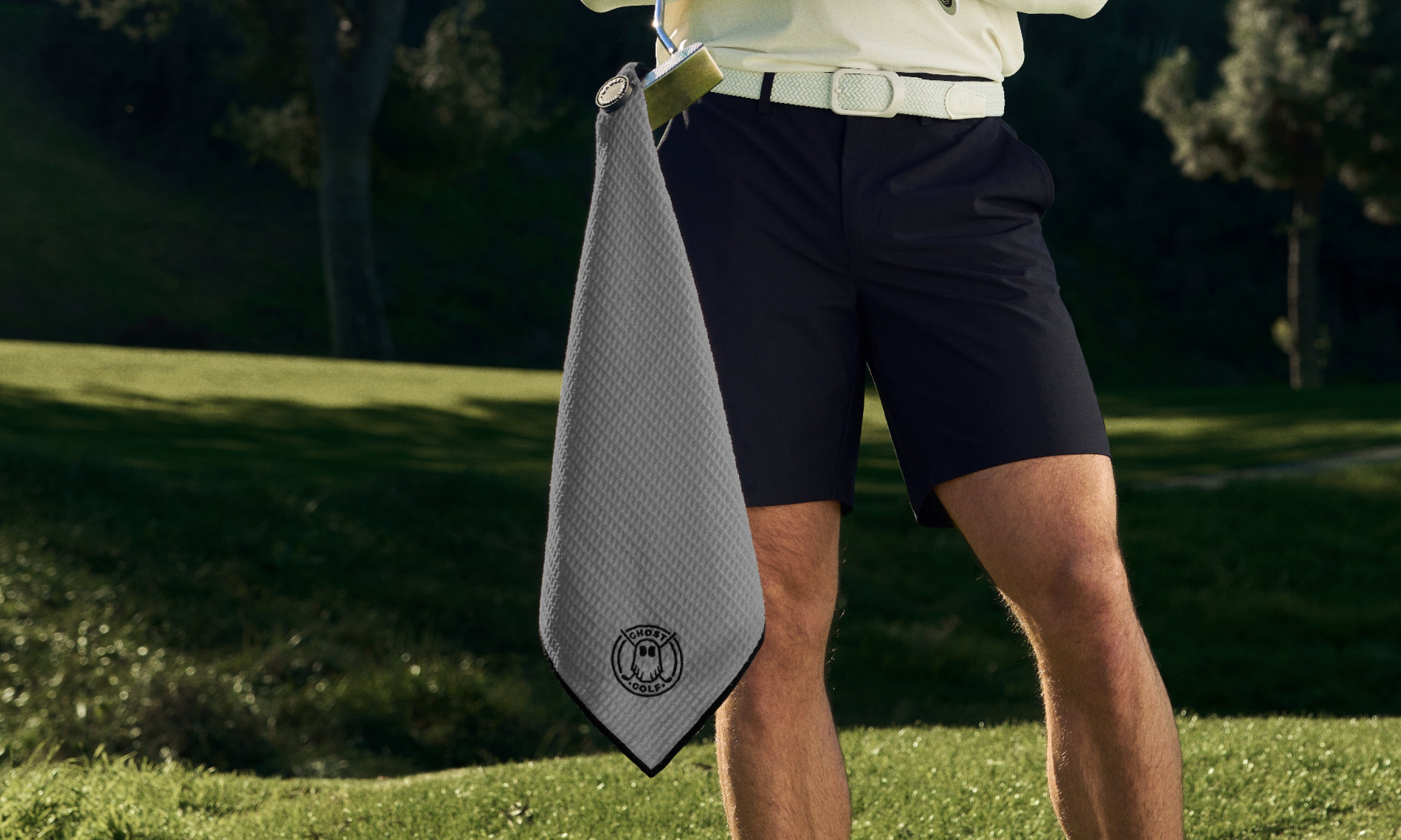 Person holding a gray golf towel with Ghost Golf logo on a golf course