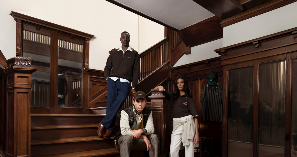 Lifestyle image of two male models and one female model sitting and standing on a staircase in a modern vintage home, looking toward the camera with relaxed, confident expressions while wearing elevated vintage-inspired outfits.