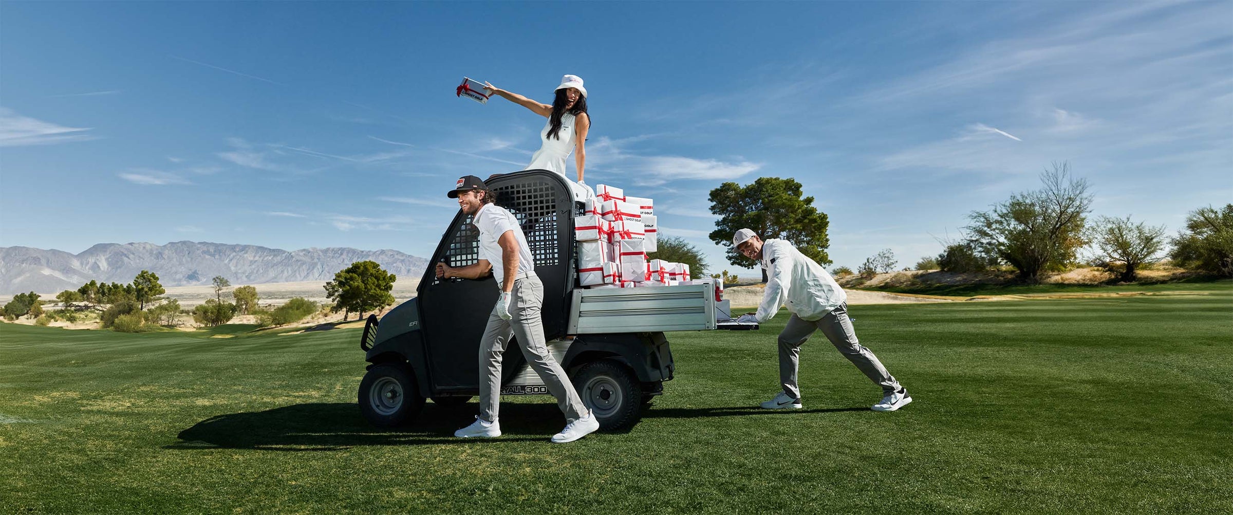 2 Men Pushing a Golf Cart with Gift Boxes and a Women on top of the cart
