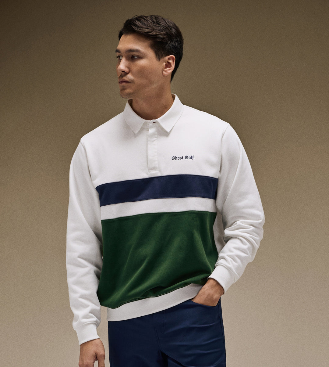 Asian Model in brown studio setting wearing a white long sleeve polo with hand in his pant pocket