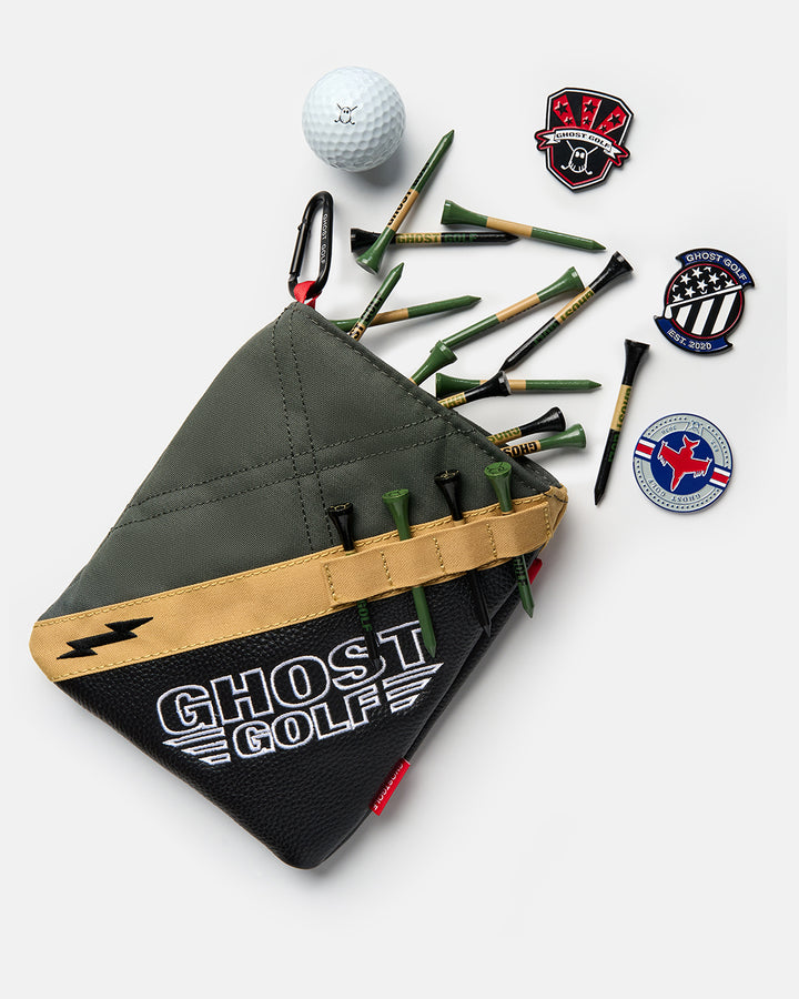 Front view of the G-Suit Utility Pouch with golf tees, ball markers, and a golf ball spilling out of the pouch. Features the Ghost Golf logo on the lower front panel, with additional golf tees secured in the dedicated tee holders on the front of the pouch. Product image highlighting the pouch's storage capacity, organization features, and premium Ghost Golf branding.