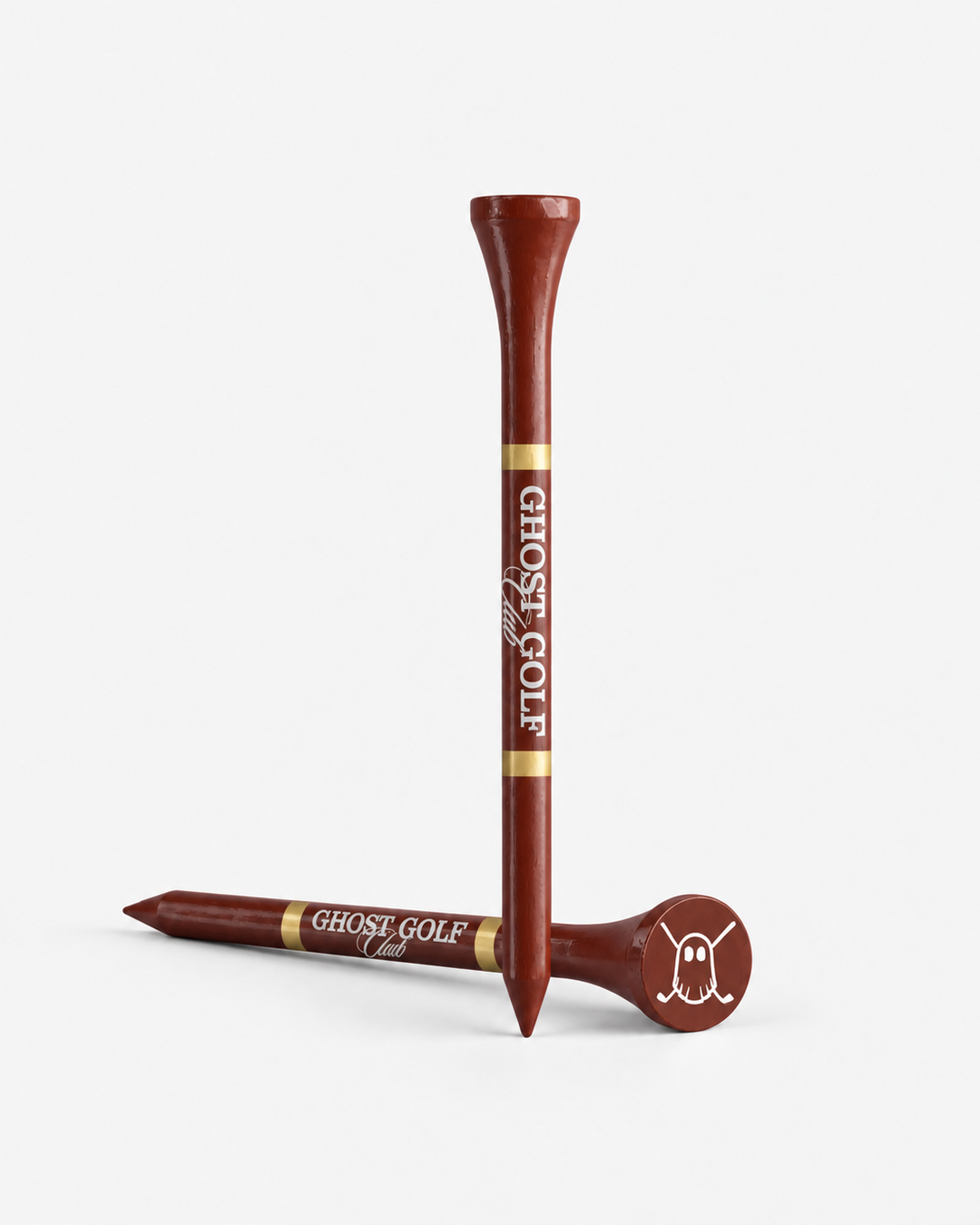 Two brown wooden golf tees with gold bands and white 'GHOST GOLF' branding, shown on a clean white background. One tee is upright with the club end labeled 'GHOST GOLF', and the other lies on its side with the ball end featuring a white ghost graphic.
