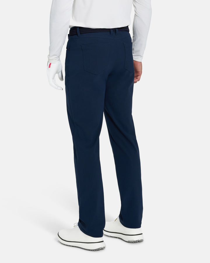 Back View of Navy Ghost Golf Core 5 Pocket Pant on White Male Model with white shoes #color_navy