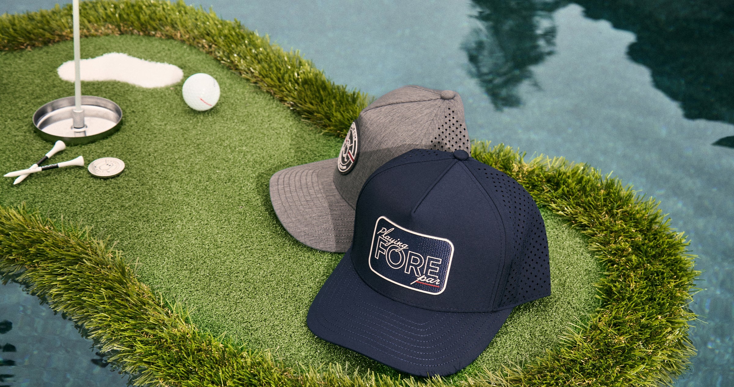Two hats rest on a golf-style mat floating in a pool, creating a stylish golf-inspired display. Golf accessories are arranged around the mat, adding to the relaxed and elevated poolside lifestyle aesthetic.