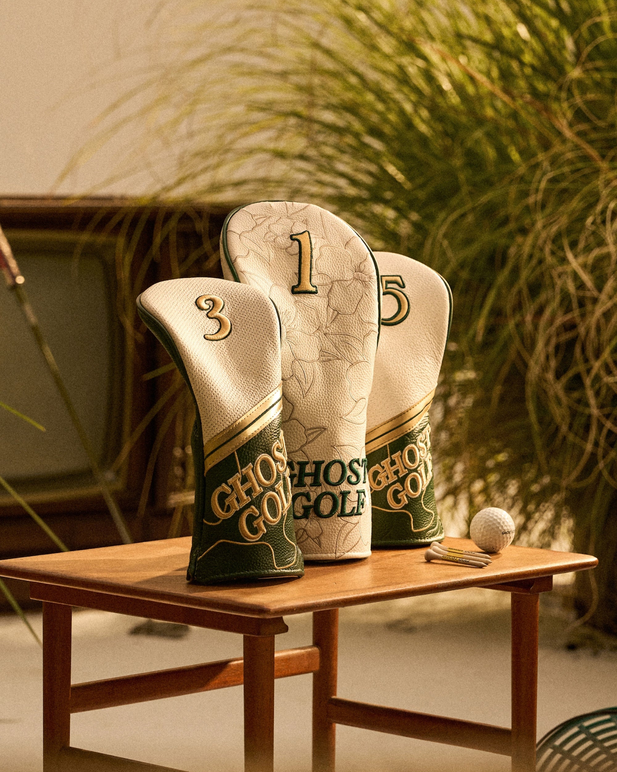 Leather Head Covers on a table with tees and golf ball in a grassy studio setting