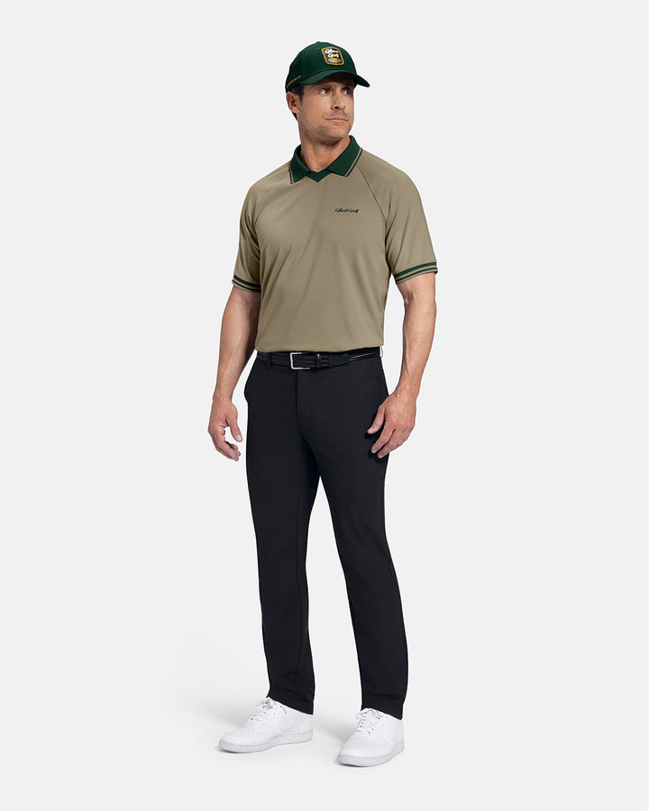 Full Body Front View of Sand Patrons Heritage Polo on white male model wearing black pants and white shoes green hat black belt with polo tucked in pants #color_sand-wedge