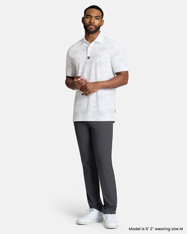 Full Body Front Shot of Black Male Model Wearing White Qualifier Argyle Polo with grey pants and white shoes. Polo is untucked. #color_white