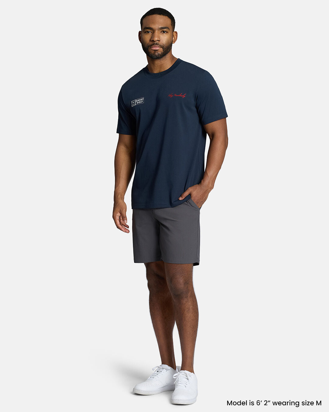 Full Body Front Shot of Black Male Model Wearing Dark Navy Qualifier Player Tee with bgrey shorts and white shoes. #color_dark-navy