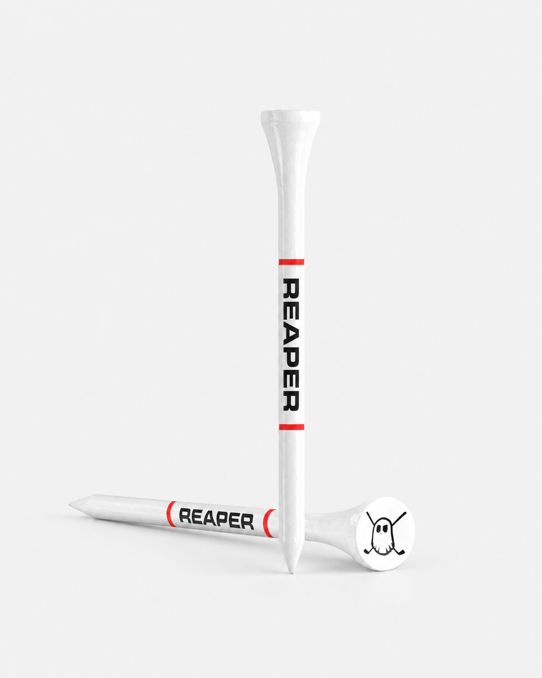 Two white tees with red bands and black 'REAPER' text, shown on a clean light gray studio background. One tee is upright and one lies on its side, with a white club head resting on the tee base.