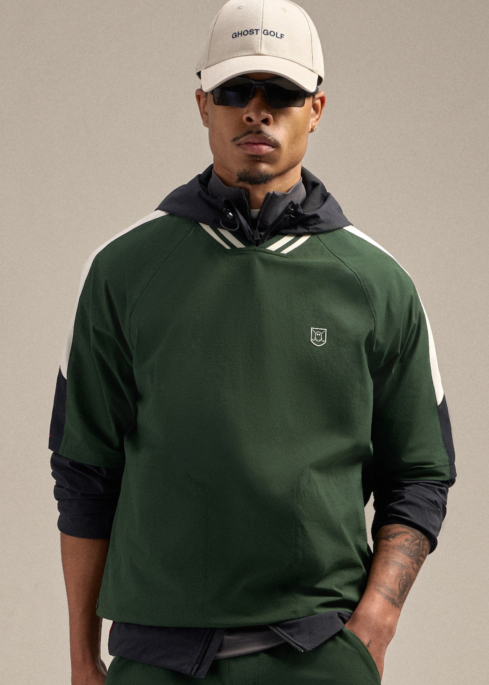 Front shot of a Black male model looking ahead, wearing a beige hat and sunglasses. He is dressed in a green fairway windshirt and matching windshorts, creating a clean and sporty golf-inspired look.