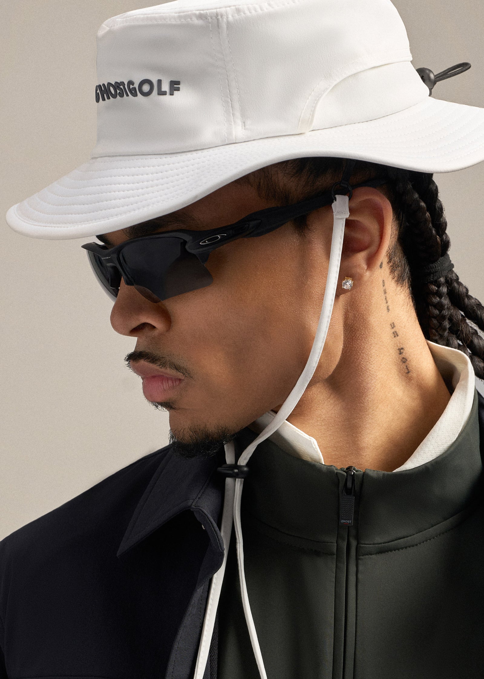 Close-up shot of a Black male model wearing a boonie hat, sunglasses, and a jacket layered over a mock neck, creating a clean and modern look.
