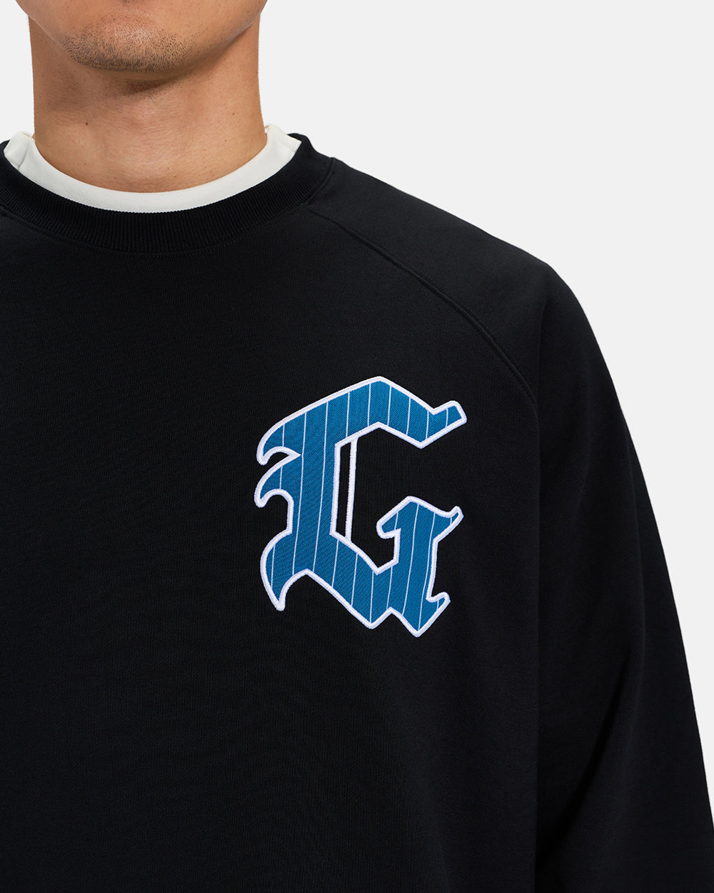 Front Closeup View of Black Spectator Raglan Sweatshirt on Asian Male Model with stylized G #color_black