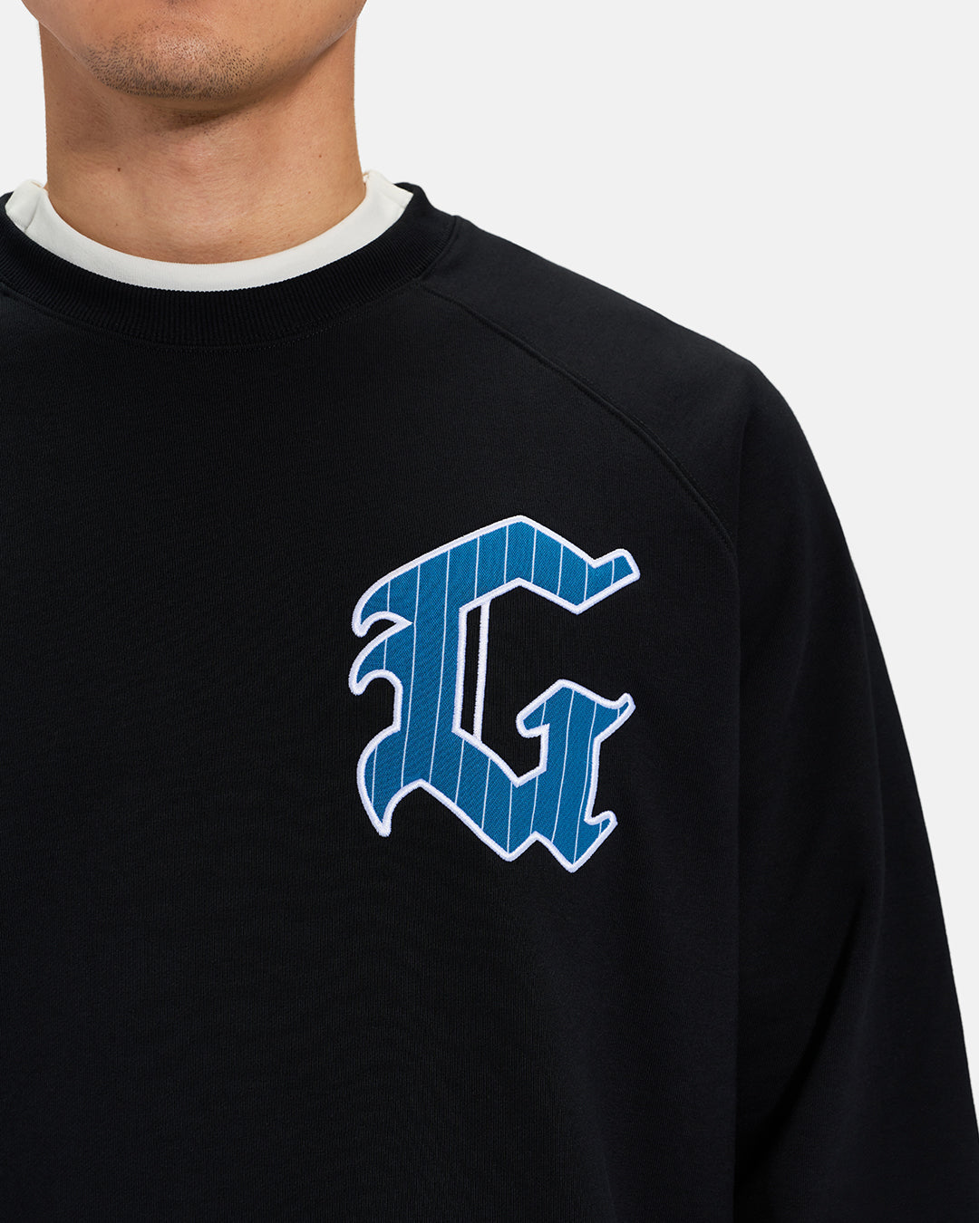 Front Closeup View of Black Spectator Raglan Sweatshirt on Asian Male Model with stylized G #color_black