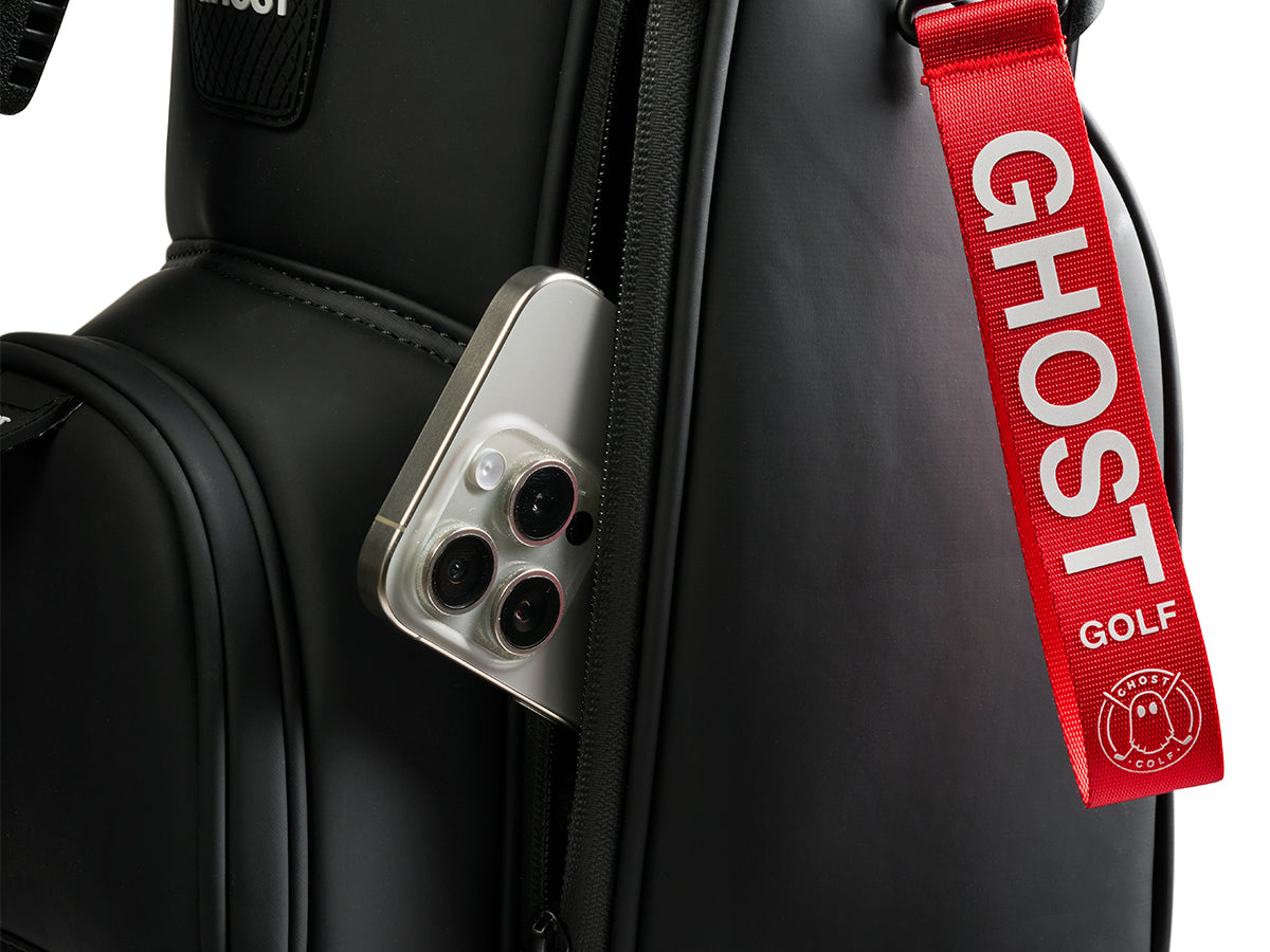 Black golf bag with a red 'Ghost Golf' strap and a phone attached.