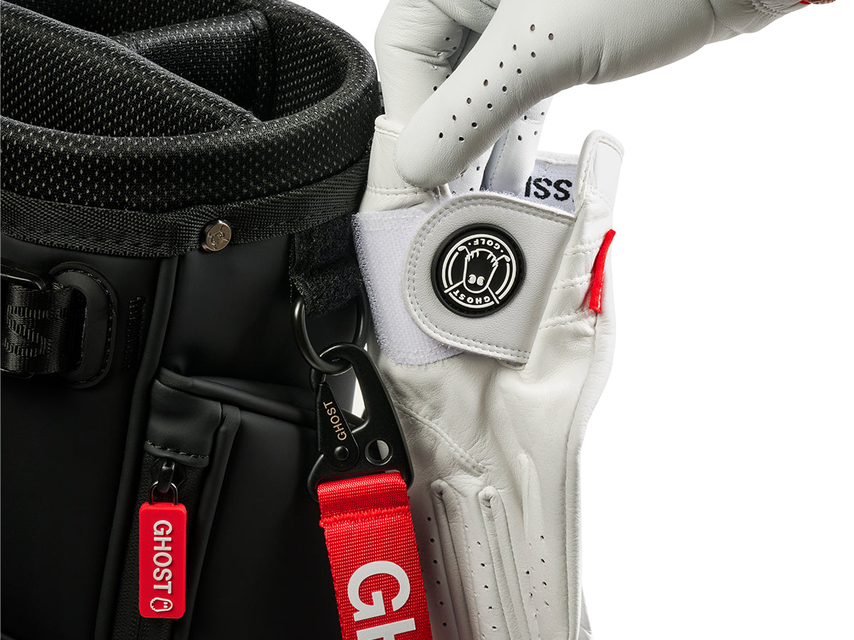 White golf glove with red strap and black logo on a black bag with red 'GHOST' branding.