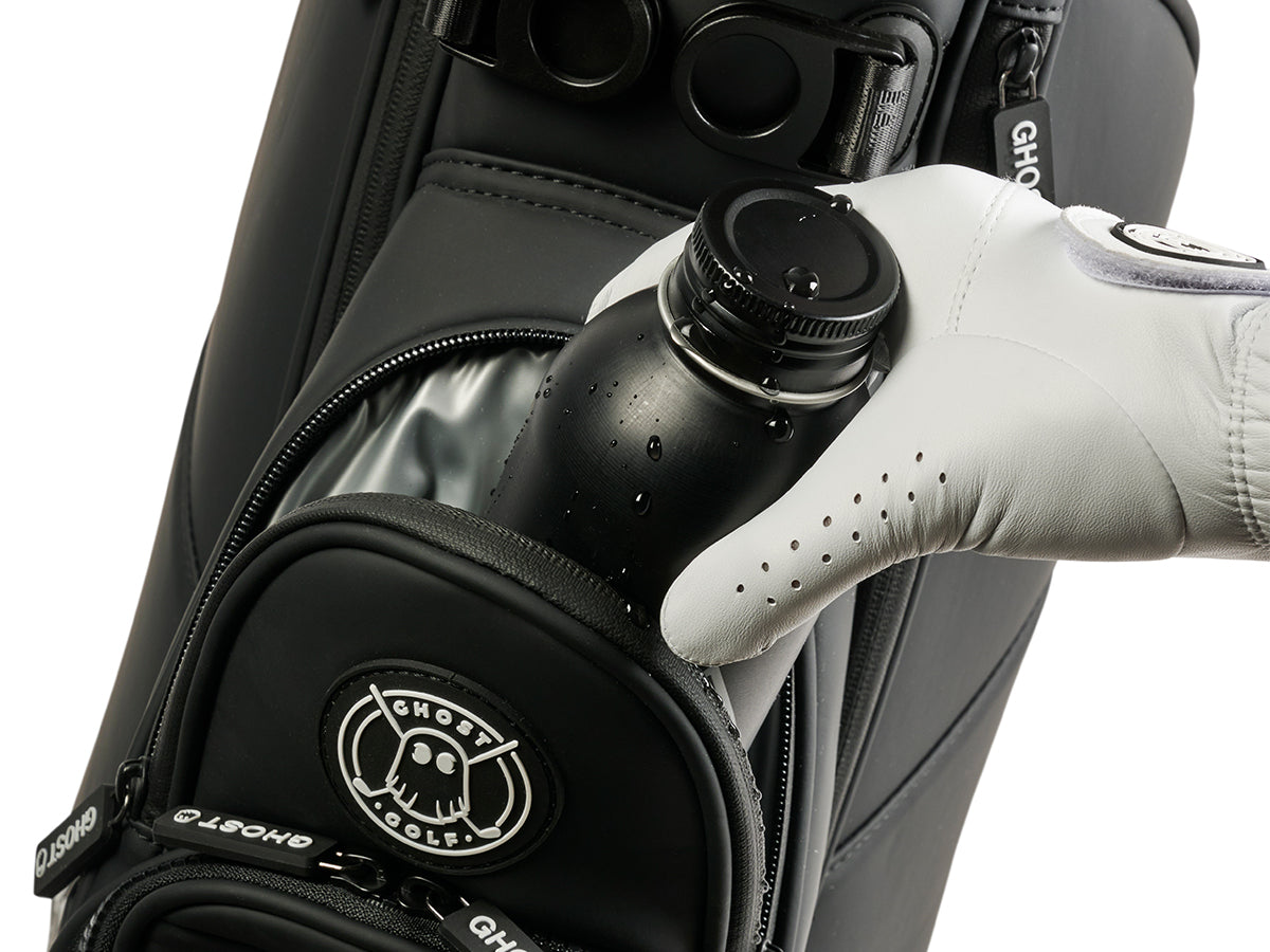 Golf bag with a black bottle being held by a gloved hand, featuring the Ghost Golf logo.