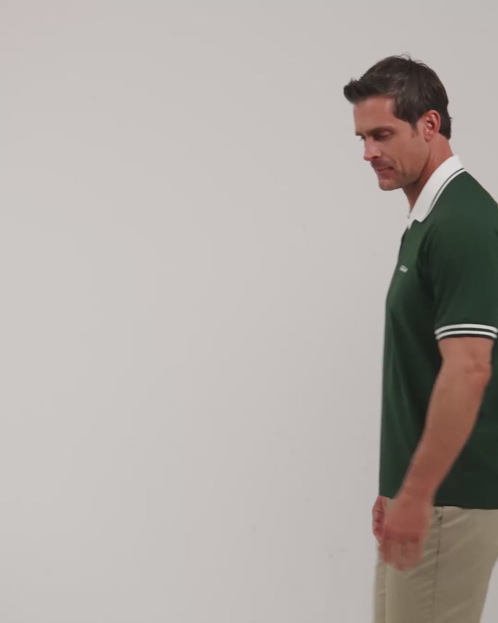 Male model walking naturally showcasing Bogey Green Patrons Heritage Polo from all angles wearing beige pants and white shoes #color_bogey-green